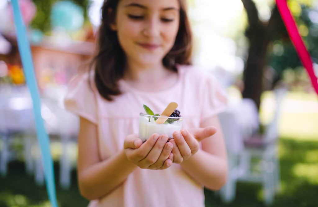 Front view of small girl outdoors in garden in summer, holding dessert in cup.