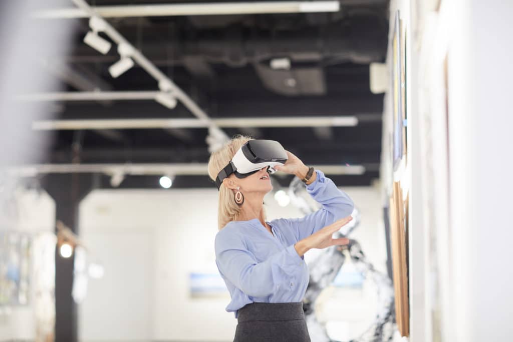 Side view portrait of elegant woman wearing VR gear while enjoying immersive experience during exhibition in art gallery, copy space