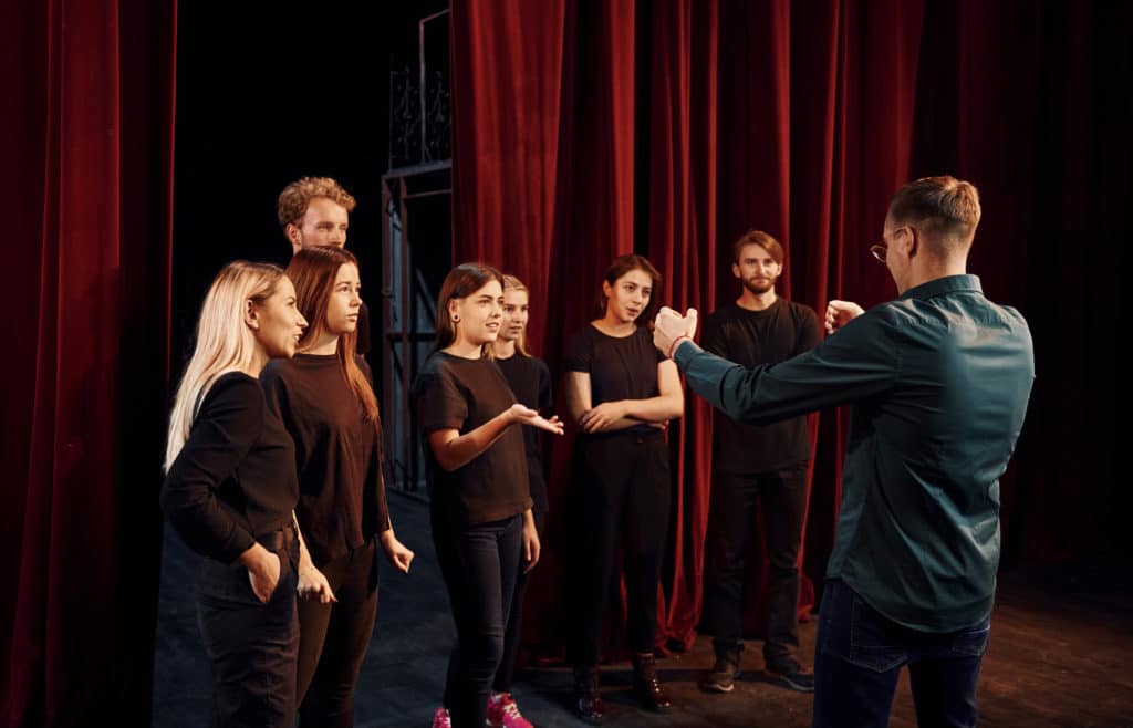Group of actors in dark colored clothes on rehearsal in the theater.